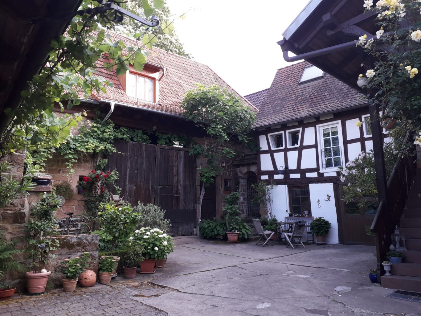 Tisch und Stühle Bänke Innenhof mit dekorativen Pflanzen, Fachwerkhäusern und einem kleinen Tisch mit Stühlen.
